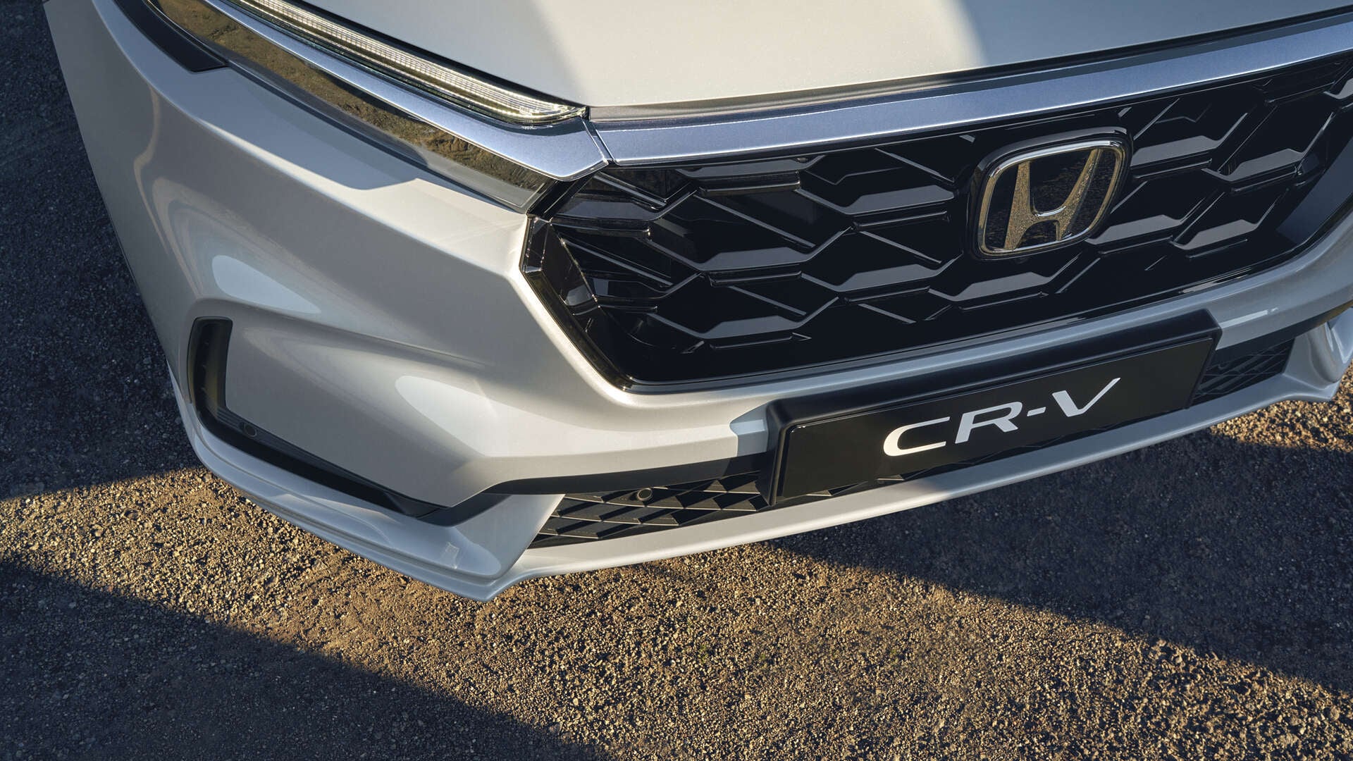 Detailný záber na prednú mriežku chladiča modelu Honda CR-V s čiernym vzorom včelieho plástu, logom Honda v strede a názvom modelu CR-V viditeľným pod ním.